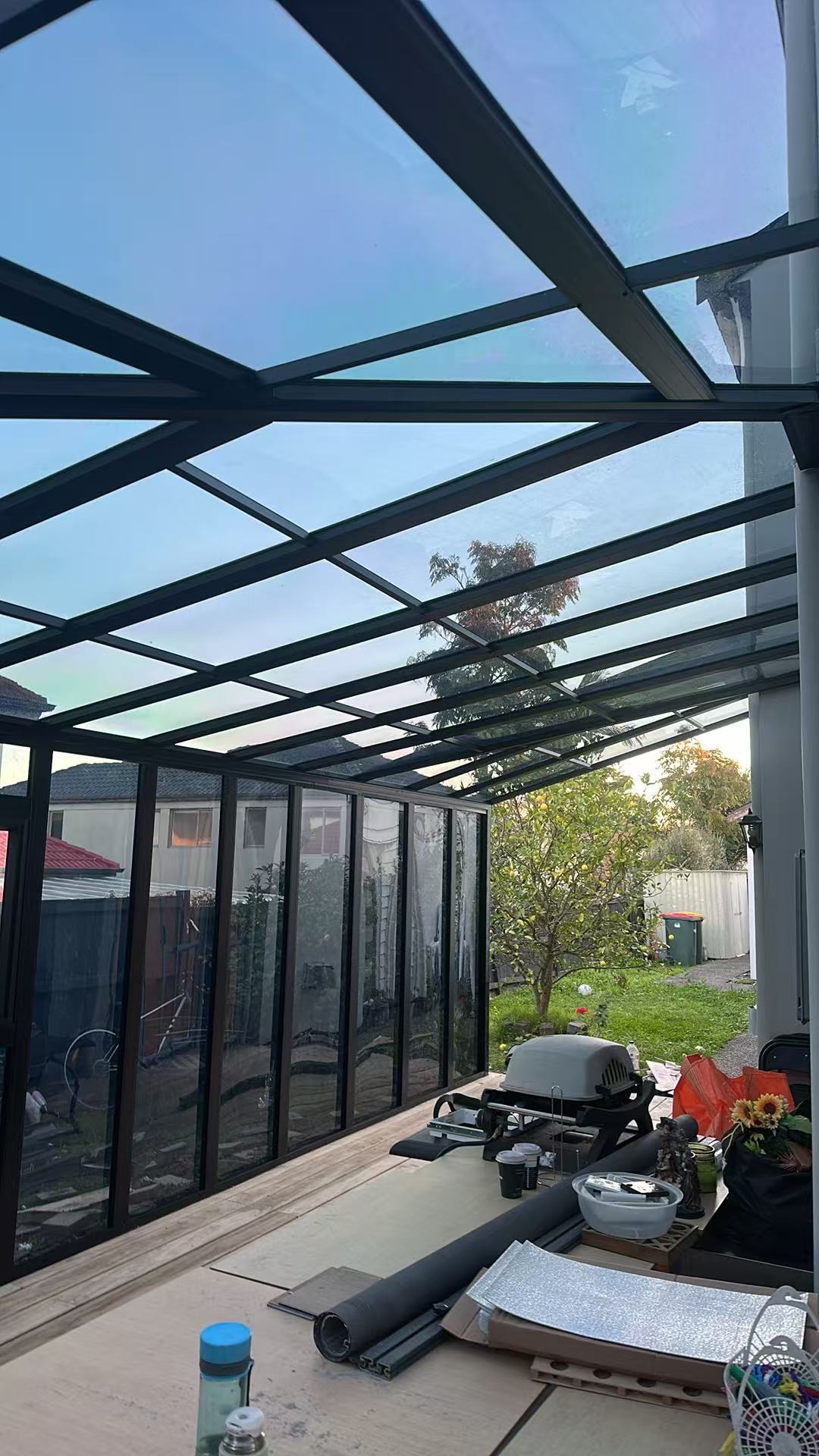 Inside a glass sunroom at dusk, iridescent glass roof